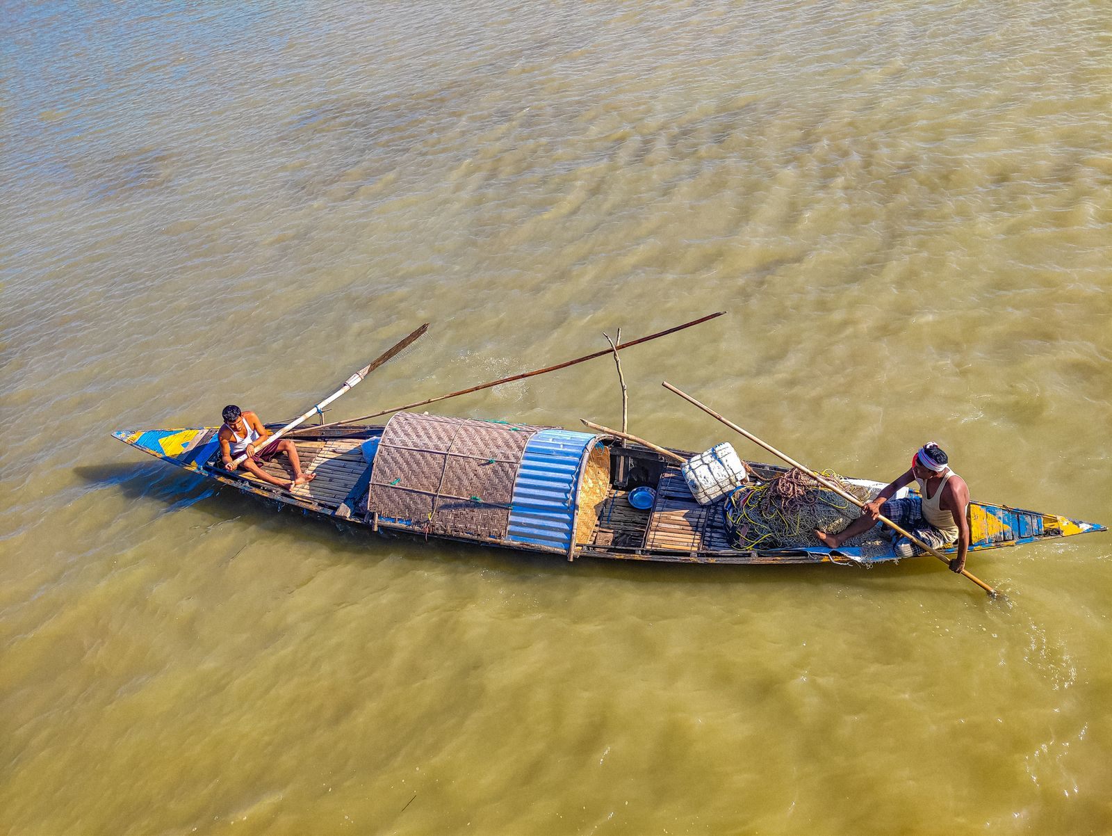 Two fishermen poling a covered wooden boat across the silty Brahmaputra in Assam, the river every Brahmaputra river cruise follows